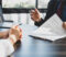 Businessman in suit in his office showing an insurance policy and pointing with a pen where the policyholder must to sign. Insurance agent presentation and consulting insurance detail to customer.