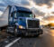 truck-accident Blue semi-truck on the highway shoulder with a damaged front bumper and scattered debris at sunset.